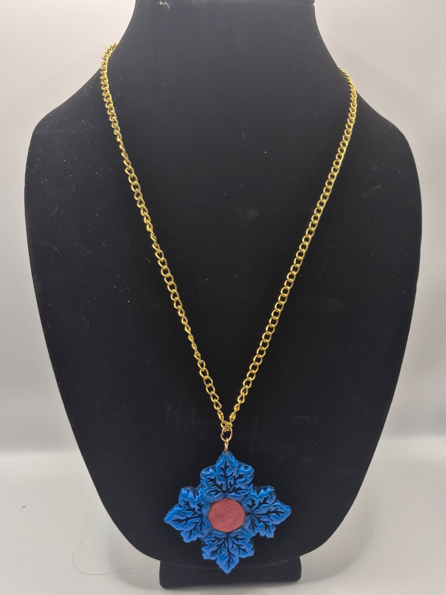 A gold chain necklace with a blue Maple leaf pendant featuring a central pink stone, displayed on a black neck mannequin bust.