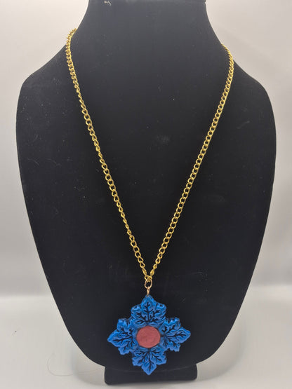 A gold chain necklace with a blue Maple leaf pendant featuring a central pink stone, displayed on a black neck mannequin bust.