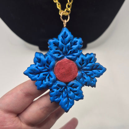 blue maple leaf pendant necklace with a red center and a gold chain, displayed against a black jewelry bust and white background.